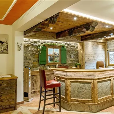 Ein gemütlicher Empfangsbereich mit rustikalen Holzmöbeln und einem Steinboden. Grüne Fensterläden und warme Beleuchtung schaffen eine einladende Atmosphäre.