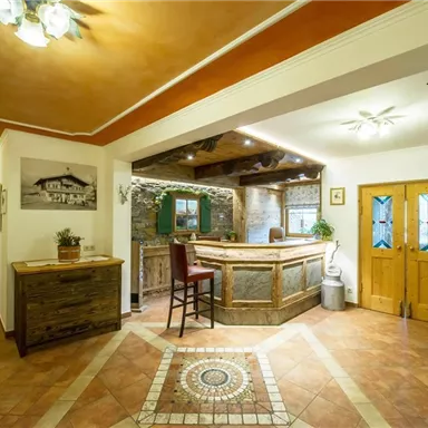 Ein einladender Empfangsbereich mit einem Holzschalter und warmen Farben. Die Wände sind mit dekorativen Elementen und Pflanzen geschmückt.