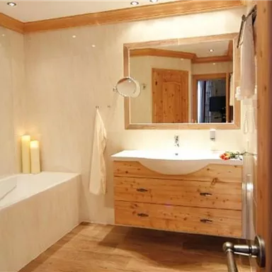 Ein modernes Badezimmer mit Holzverkleidungen und einem großen Spiegel. Es gibt eine Badewanne und ein Waschbecken mit gepflegter Einrichtung.