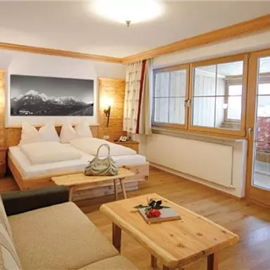 Ein gemütliches Zimmer mit zwei Einzelbetten und einem Sofa. Große Fenster sorgen für viel Tageslicht und einen Blick ins Freie.