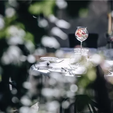 Ein eleganter Tisch in einem Restaurant, umgeben von Pflanzen. Auf dem Tisch steht ein großes Glas mit Früchten.