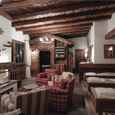 Eine gemütliche Wohnstube mit Holzvertäfelung und einem Kamin. Es gibt bequeme Sessel, ein rustikales Ambiente und große Fenster.