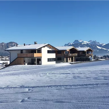 Ein modernes Gebäude in einer verschneiten Landschaft. Im Hintergrund sind Berge unter einem klaren blauen Himmel zu sehen.