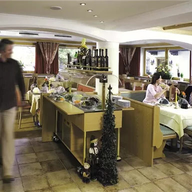 Ein gemütliches Restaurant mit holzvertäfelten Tischen und Dekoration. Zwei Frauen sitzen am Tisch und genießen ihre Getränke, während ein Mann vorbeigeht.