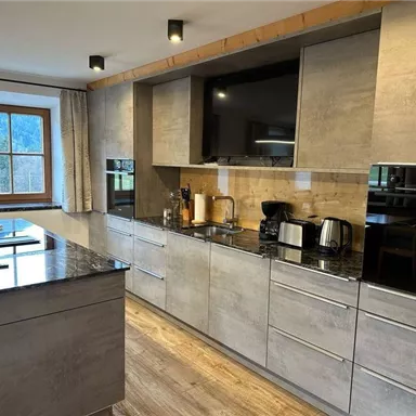 Eine moderne Küche mit grauen Schränken und einem Granitarbeitsplatz. Die Küche ist gut ausgestattet mit Geräten und hat ein Fenster, das Licht hereinlässt.