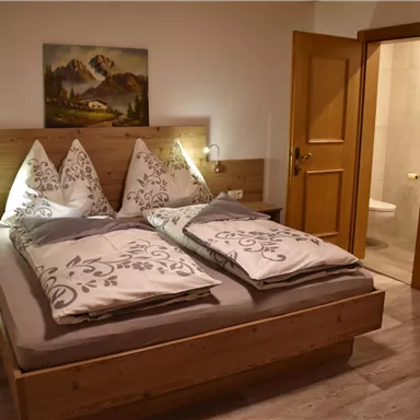 A cozy bedroom with a large double bed and wood paneling. The walls are light, and a door leads to a bathroom.