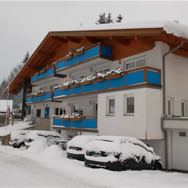 Ein modernes Wohngebäude im Schnee mit blauen Balkonen. Die Umgebung ist winterlich und ruhig.