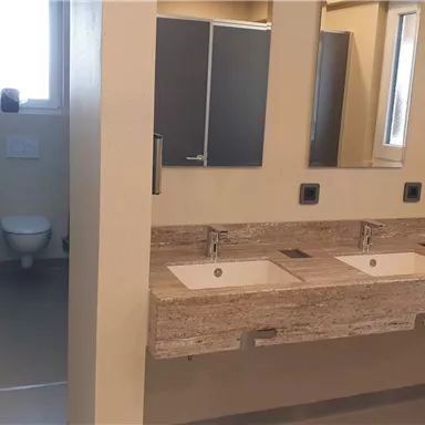 A modern bathroom with two sinks and large mirrors. In the background, separate toilet rooms can be seen.