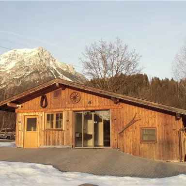 A wooden house with large windows and a beautiful mountain in the background. Snow lies in front, and the landscape is calm and idyllic.