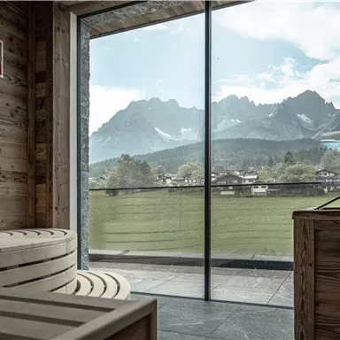 Ein modernes Spa mit einer Holzsauna und großen Fenstern. Der Blick zeigt majestätische Berge und eine grüne Landschaft.