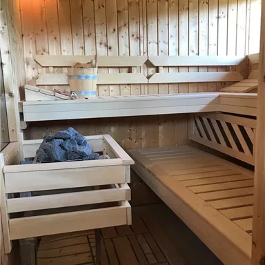 A traditional sauna made of wood with benches and a water container for infusions. The walls are made of light, polished wood and there is a relaxing atmosphere.