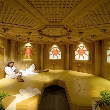 A relaxing spa with wooden paneling and colorful windows. A person in a bathrobe is comfortably lying on a lounger.