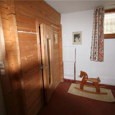 A room with wood paneling and a wooden rocking horse. Curtains hang on the wall and a framed picture is visible.