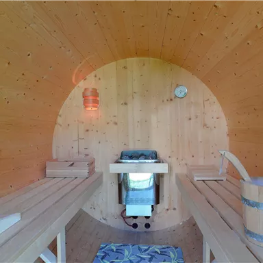 A cozy wooden sauna room with benches and a tranquil atmosphere. In the middle, there is a stove and a wooden bucket.