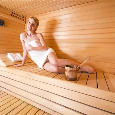 A relaxed person is sitting in a wooden sauna. They are wearing a towel and enjoying the peace and warmth.