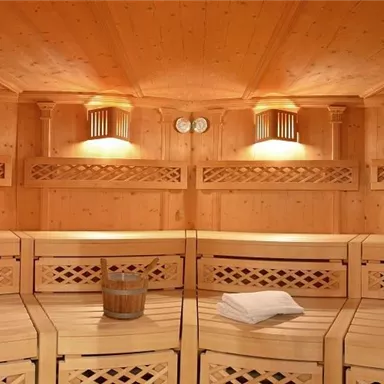 Ein gemütlicher Saunabereich mit Holzverkleidung und sanfter Beleuchtung. Zwei Salzlampen und eine Holzbank bieten eine entspannende Atmosphäre.