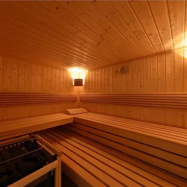 Eine gemütliche Sauna mit Holzverkleidung und Bänken zum Entspannen. Das warme Licht sorgt für eine beruhigende Atmosphäre.