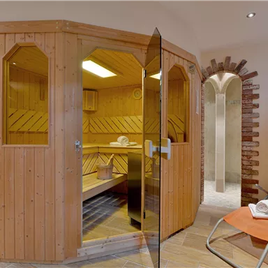 Ein gemütlicher Saunabereich mit Holzverkleidung und Glas Tür. Neben der Sauna befindet sich ein orangefarbener Liegestuhl.