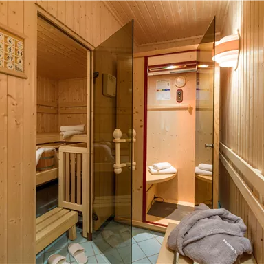 A cozy sauna room with wooden paneling and soft towels. The glass door opens the way to a modern steam shower.