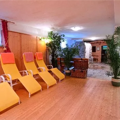 Ein entspannender Wellnessbereich mit gelben Liegen und grünen Pflanzen. Die Holzverkleidung und der Steinboden schaffen eine gemütliche Atmosphäre.