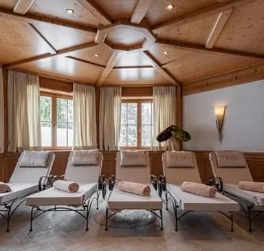 Ein heller Wellnessbereich mit mehreren Liegen und großen Fenstern. Die Wände sind aus Holz, was eine gemütliche Atmosphäre schafft.