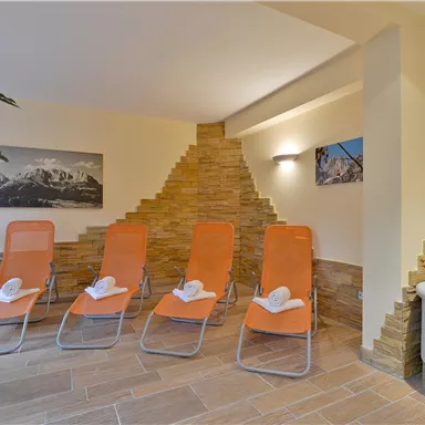 Ein entspannender Wellnessbereich mit orangefarbenen Liegen und einem modernen Brunnen. Die Wände sind mit Stein gestaltet und vermitteln eine ruhige Atmosphäre.