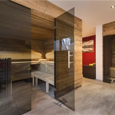 A modern sauna interior with wooden paneling and clear glass doors. The atmosphere is relaxed and inviting.
