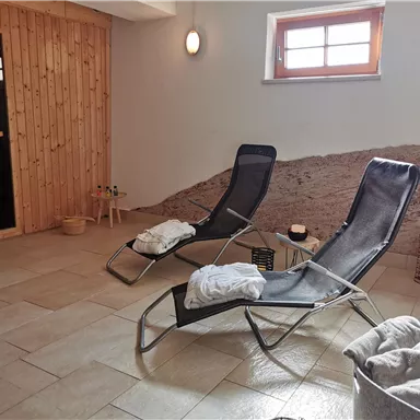 A relaxing wellness area with loungers and soft lighting. The wood paneling and door area create a cozy atmosphere.