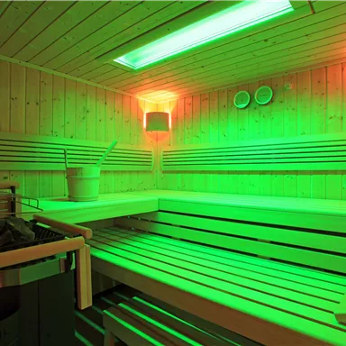 Eine beeindruckende Sauna mit grünen Lichtakzenten und Holzbank. Der Raum strahlt Entspannung und Wellness aus.