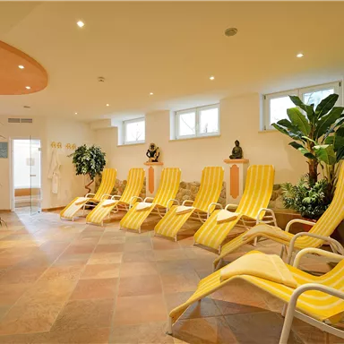 A relaxing wellness area with yellow loungers and lush plants. Soft light creates a calm atmosphere.