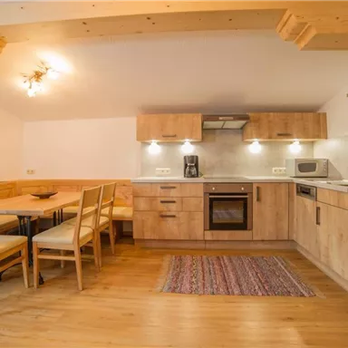 A modern kitchen with wooden furniture and a dining area. The equipment includes a stove, a microwave, and a dining table with chairs.