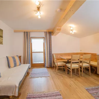 A cozy living space with a sofa, a dining area, and a modern kitchen. Bright colors and wooden details create an inviting atmosphere.