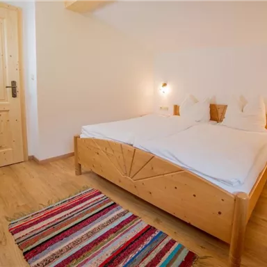 A cozy bedroom with a double bed and wooden details. The room has a warm, inviting carpet and a wooden door.