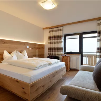 Ein gemütliches Zimmer mit einem großen Doppelbett und Holzverkleidung. Es gibt ein Fenster mit Blick nach draußen und eine Couch.