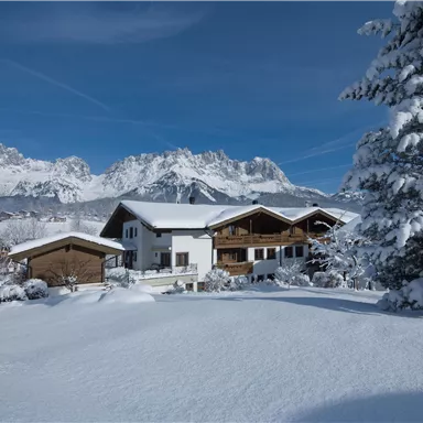 A picturesque winter landscape with snow-covered hills and mountains in the background. The wooden houses rest gently in the snow and radiate coziness.