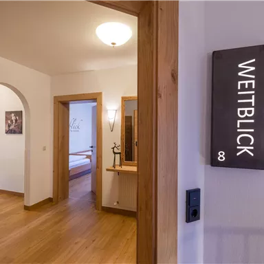 An inviting hallway with wood paneling and a sign that reads "WEITBLICK." In the background, a room with a cozy atmosphere is visible.