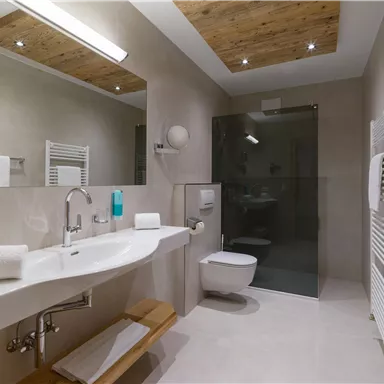 A modern bathroom with a spacious shower and bright, neutral colors. Wood details give the room a warm atmosphere.