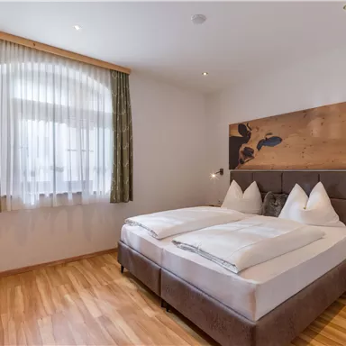 A cozy bedroom with a large double bed and wooden floor. The window lets in plenty of daylight and creates an inviting atmosphere.