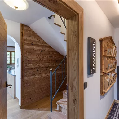 An inviting hallway with wooden details and a staircase. Shelves with various materials hang on the wall.