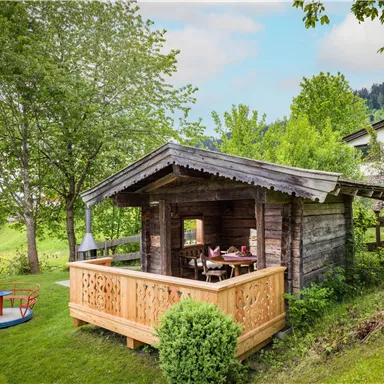 A cozy wooden house surrounded by green nature. In the foreground, there is a small playground.