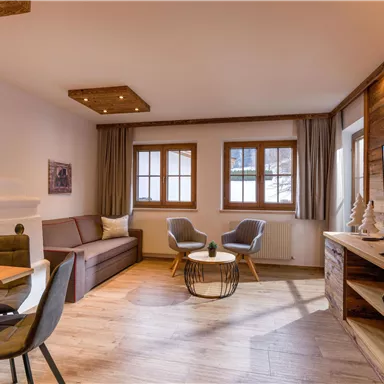 A cozy living and dining room with modern furniture and wooden decor. Large windows let in plenty of light and offer a view outside.