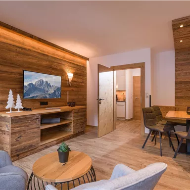 A modern living room with wooden paneling and cozy furnishings. A television and a dining table complete the warm atmosphere.