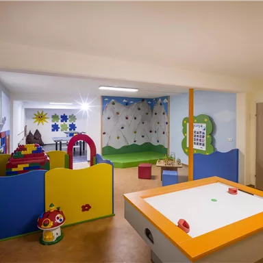A colorful playroom with various play areas and a climbing wall. There are many colorful pieces of furniture and toys.