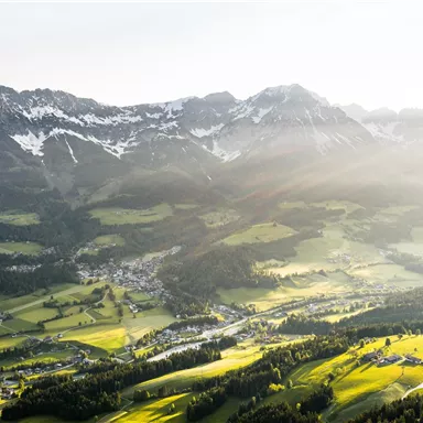 A picturesque mountain landscape with snow-capped peaks and green valleys. The sun is shining and illuminating the surroundings.