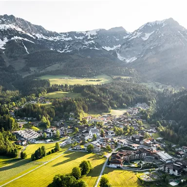 A picturesque mountain landscape with snow-covered peaks and a tranquil village. Lush meadows and forests surround the settlement.