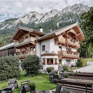 A charming wooden house with balconies, surrounded by green nature and mountains in the background. The quiet atmosphere invites relaxation.