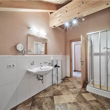 A modern bathroom with a shower, a sink, and large tiles. The walls are painted in neutral tones, and the wooden ceiling gives the space a warm atmosphere.