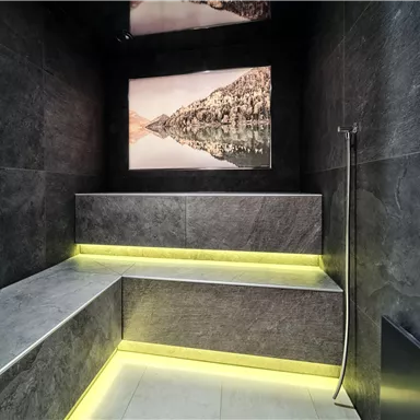 A modern steam room with dark walls and elegant lighting elements. A picture of a tranquil landscape hangs on the wall.