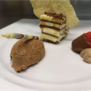A plate with various desserts: chocolate mousse, a layer cake, and a chocolate-covered strawberry bite. The decoration includes a colorful chocolate stripe.