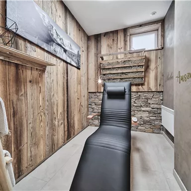 A modern room with a black lounge and wooden paneling. The walls are designed in a rustic style, creating a cozy atmosphere.